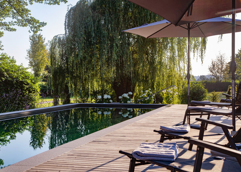 Holzterrasse mit stilvollen Stühlen und Schirmen, beim Naturpool des Hotel Quellenhof.