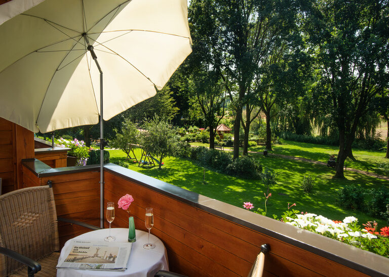 Ein weißer Schirm bei einem Tisch in der Sonne auf der Terrasse mit Blick auf den Garten - Doppelzimmer Komfort Südlage.