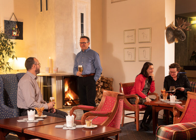 Gemütlicher Gästeabend in der Lobby des Hotel Quellenhof, mit Getränken und Gesprächen vor dem brennenden Kamin.