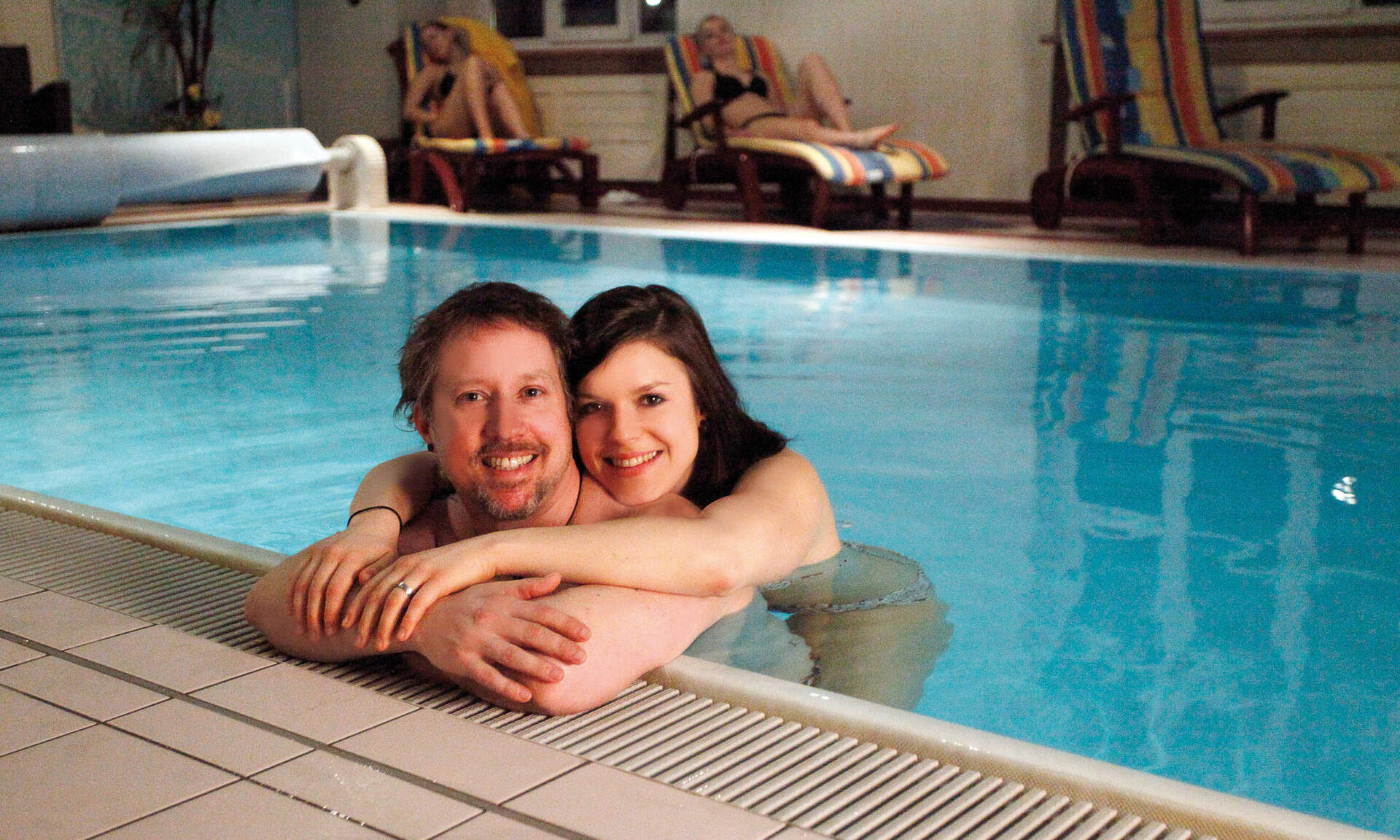 Eine glückliches Paar am Beckenrand im Schwimbecken der Hausthereme des Hotels.