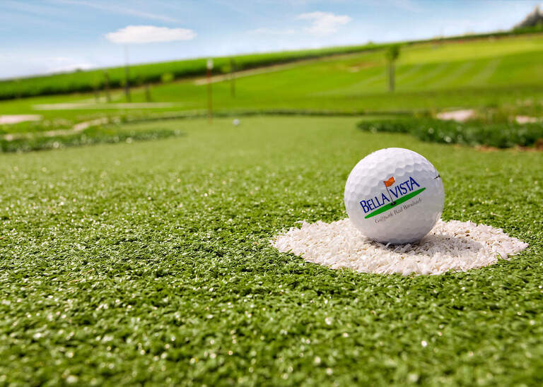 Ein Golfball mit Bella-Vista Golfpark Logo liegt zum Abschlag bereit.