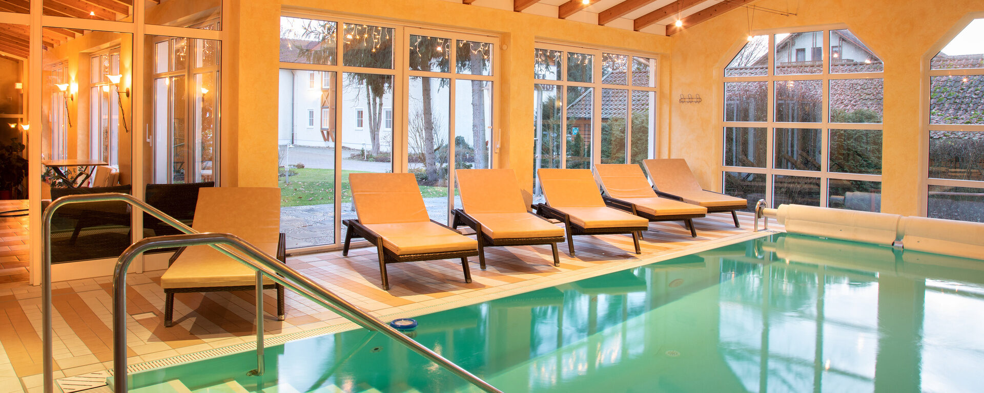 Beheizter Indoor Pool mit Liegen vor einer hellen Fensterfront im Hotel Quellenhof in Bad Birnbach.