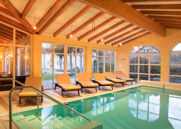 Beheizter Indoor Pool mit Liegen vor einer hellen Fensterfront im Hotel Quellenhof in Bad Birnbach.