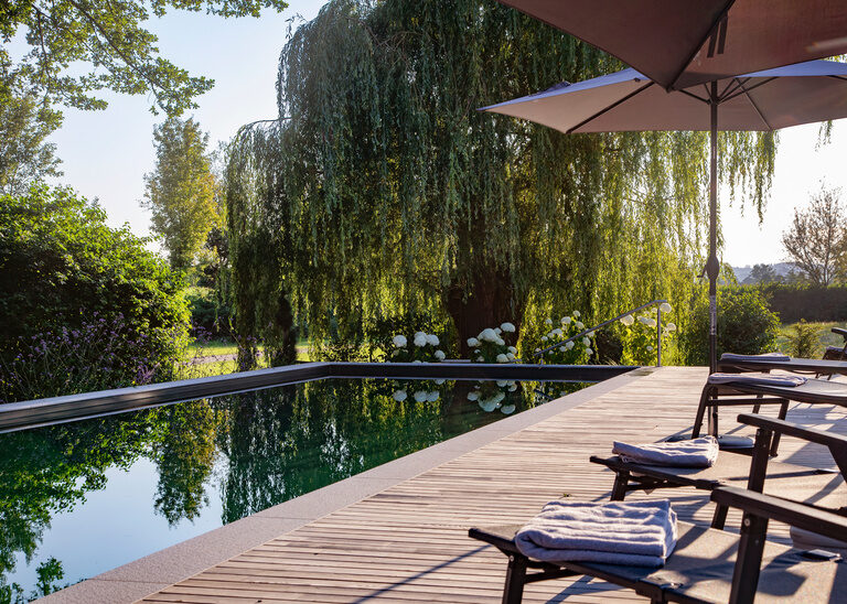 Die Holzterrasse mit Liegen und Sonnenschirmen beim Naturpool im Hotel Quellenhof im Rottal