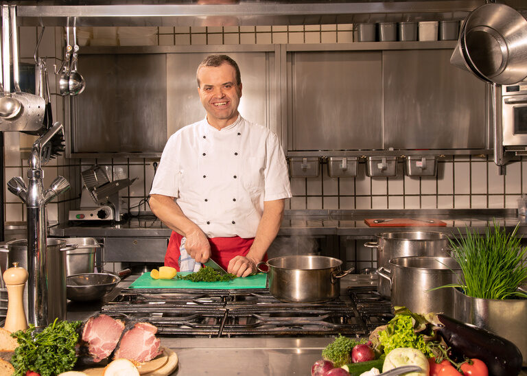 Lächelnder Küchenchef beim Schneiden und vorbereiten der Speisen in der Hotelküche des Restaurant im Quellenhof.