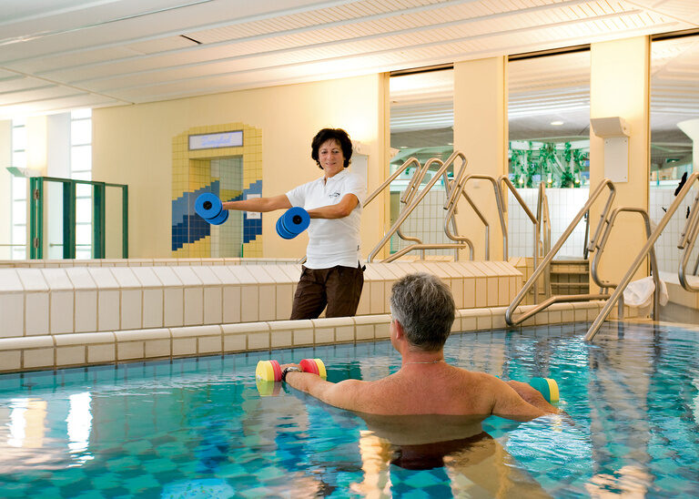 Ein Mann in einem Becken in der Rottal Terme führt Medical Wellness Übungen mit einer Trainerin aus.