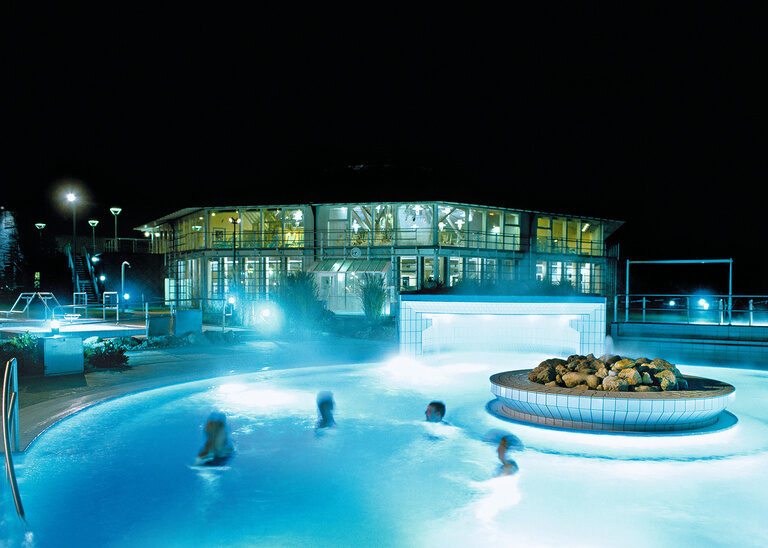 Das beleuchtete Aussenbecken der Rottal Terme bei Nacht, mit schwimmenden Besuchern.