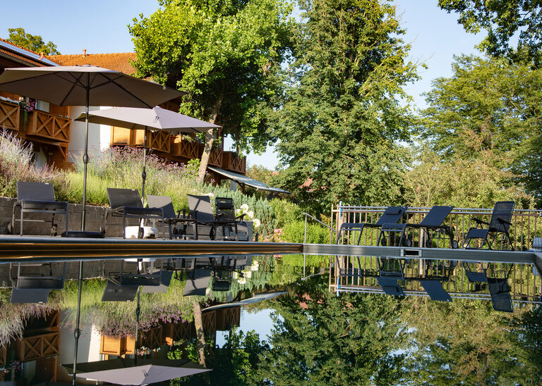 Das Spiegelbild des Hotels Quellenhof im Wasser des Naturpools.