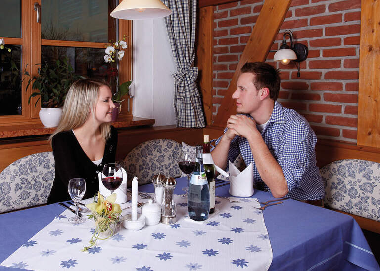 Glückliches Paar trinkt Wein und unterhält sich beim Dinner im elegant eingerichteten Quellenhof-Restaurant