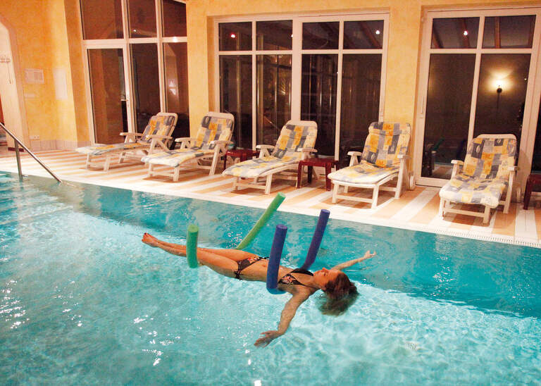 Eine Frau mit Poolnudel im Hotel Quellenhof treibt im Wasser des Innenpools.