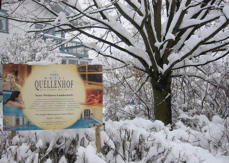 Ein Werbeschild des Hotel Quellenhof Bad Birnbach in einer winterlichen Landschaft mit viel Schnee.