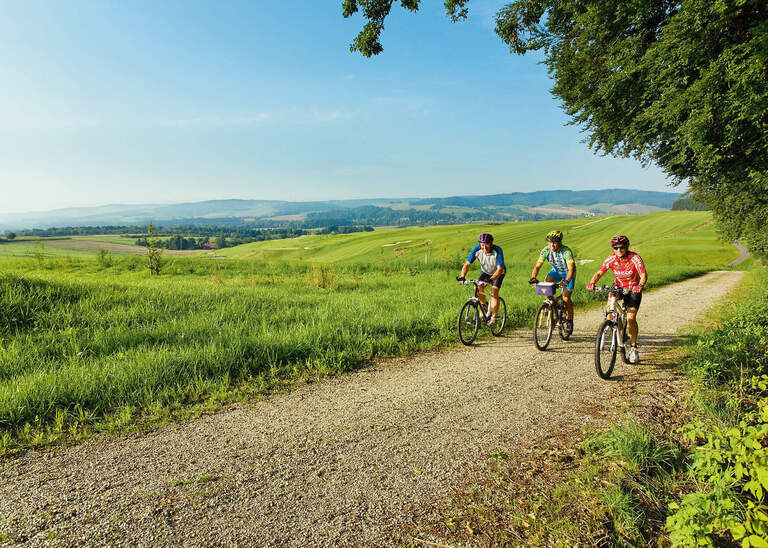 Drei Radfahrer fahren einen Weg entlang mit malerischer rottaler Landschaft im Hintergrund an einem schönen Sommertag.