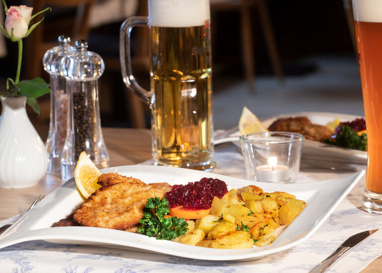 Deftiges Schnitzel Wiener Art mit Preiselbeeren und Bratkartoffeln, dazu einen Krug Bier.