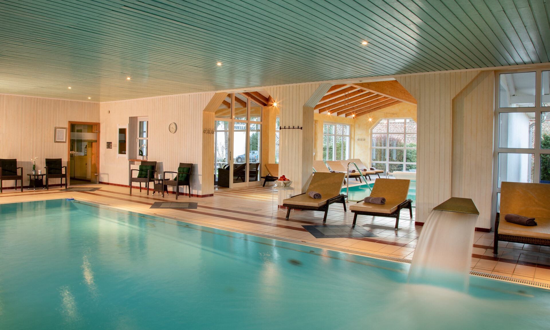 Indoor Pool im Wellnessbereich, mit Liegen und hellen, großen Fenstern im Hotel Quellenhof.