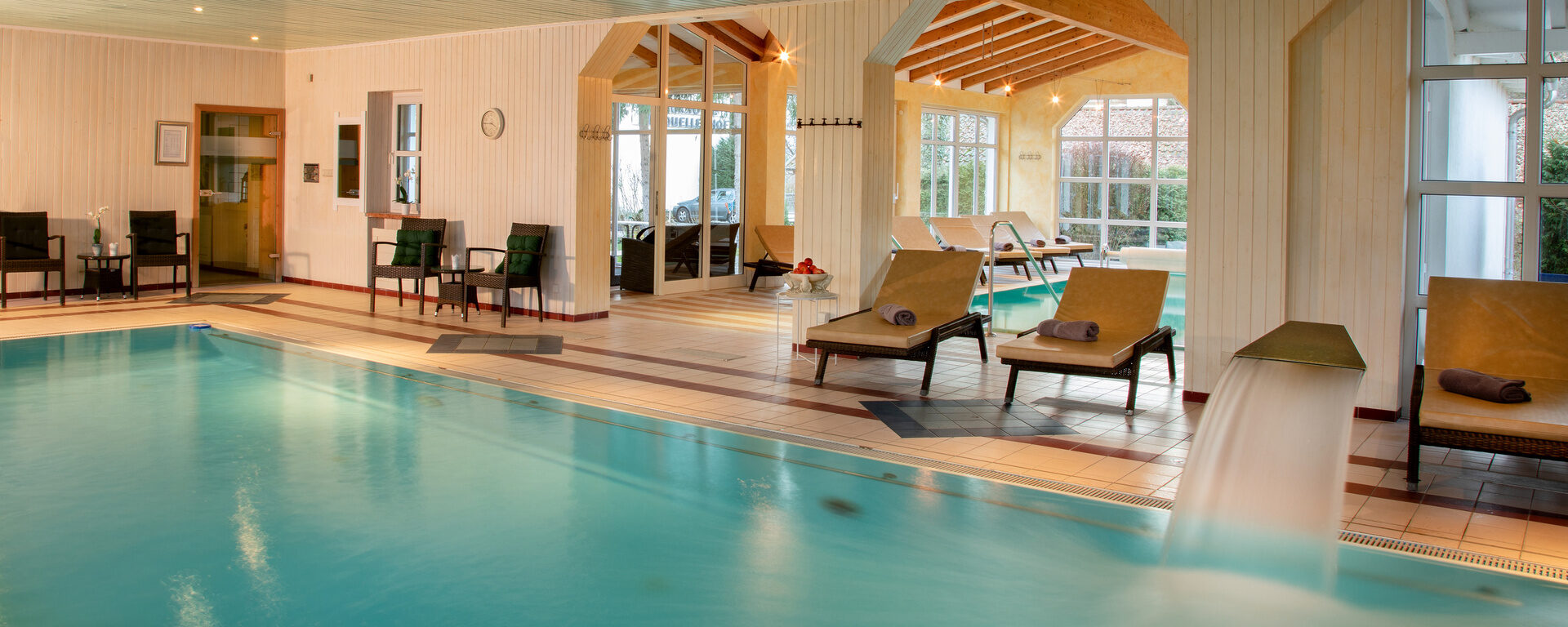 Indoor Pool im Wellnessbereich, mit Liegen und hellen, großen Fenstern im Hotel Quellenhof.