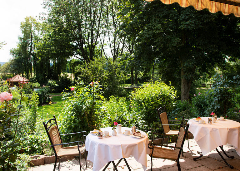 Sonnenterrasse mit angrenzenden Garten, gedeckten Tischen zum gemütlichen Sitzen und Genießen.