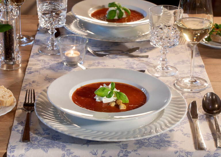 Schön garnierte Tomatensuppe auf weissen Teller mit einem Glas Weisswein im Restaurant Quellenhof.