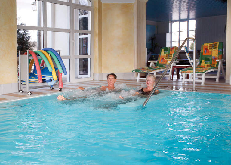 Zwei Personen liegen entspannt im Whirlpoolbereich in der Haustherme des Hotels Quellenhof Bad Birnbach.